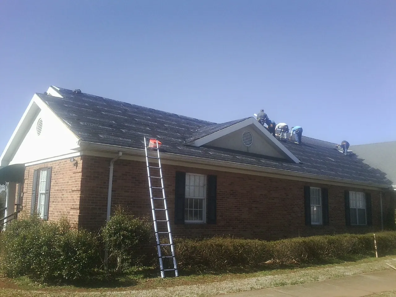 Crew tearing shingles off a brick ranch roof with a ladder set — Metal Roof Repair work by our crew in Whitinsville