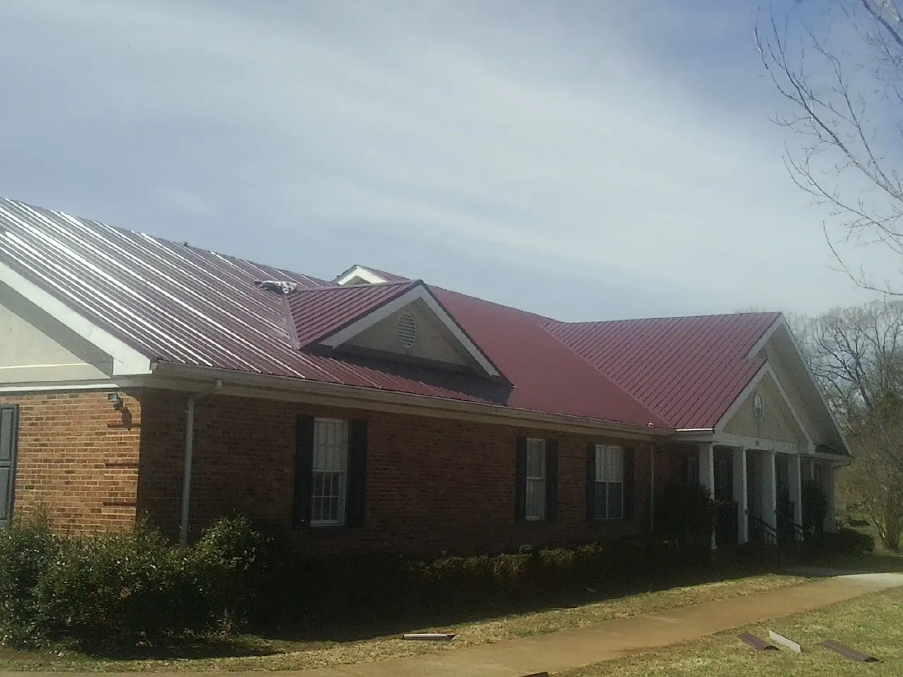 Red metal roof with gabled entries on a long brick building, from a Hail Damage Roof Repair job in Whitinsville