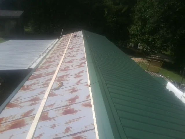Old rusted panels beside newly installed green metal roofing — Wind Damage Roof Repair by Roofing Brothers in Whitinsville