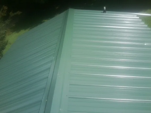 New green metal panels meeting at the ridge of a roof — Flat Roof Repair work by our crew in Whitinsville