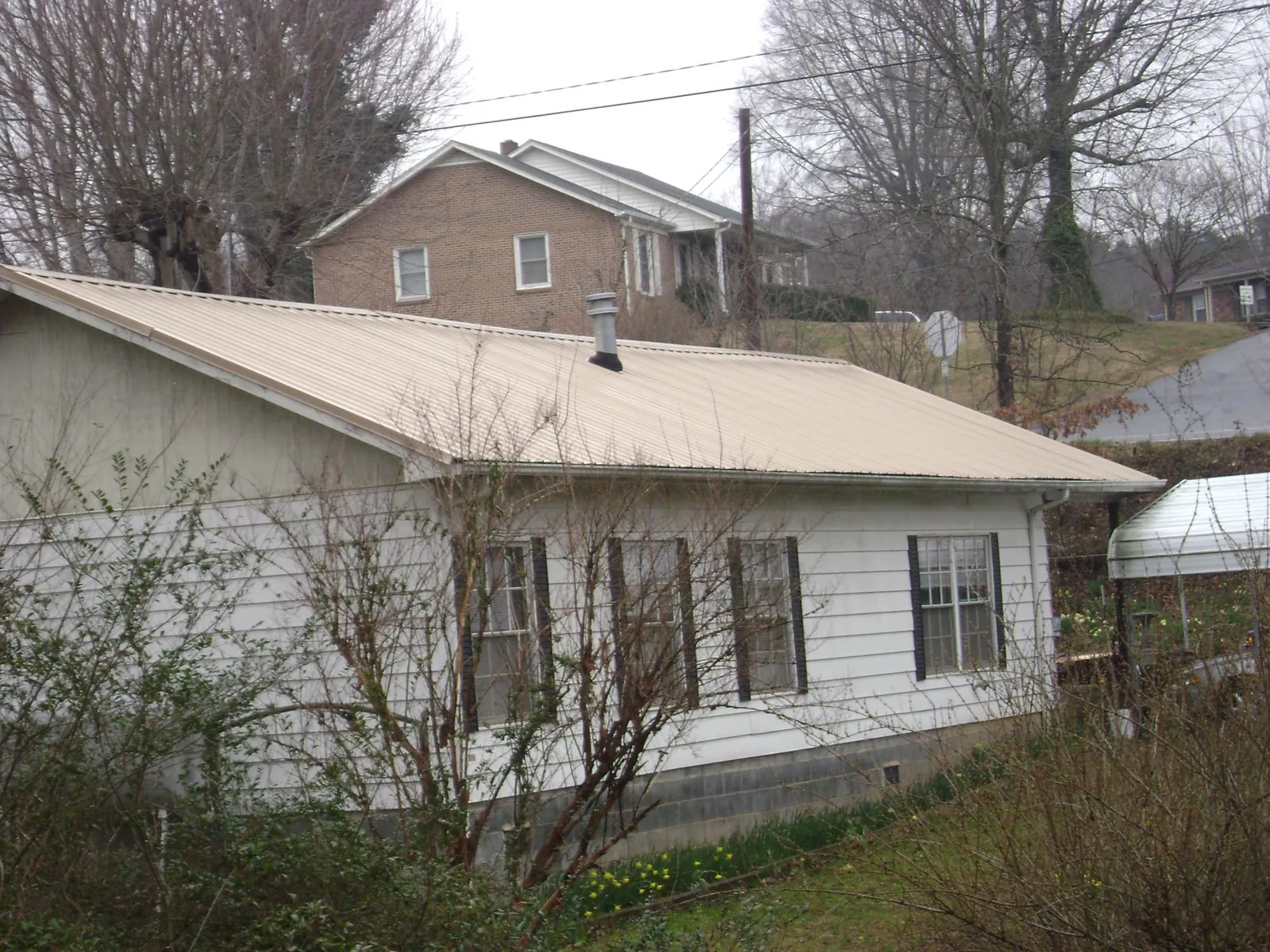 Tan metal roof on a white sided house set into a hillside — Commercial Roofing by Roofing Brothers in Whitinsville
