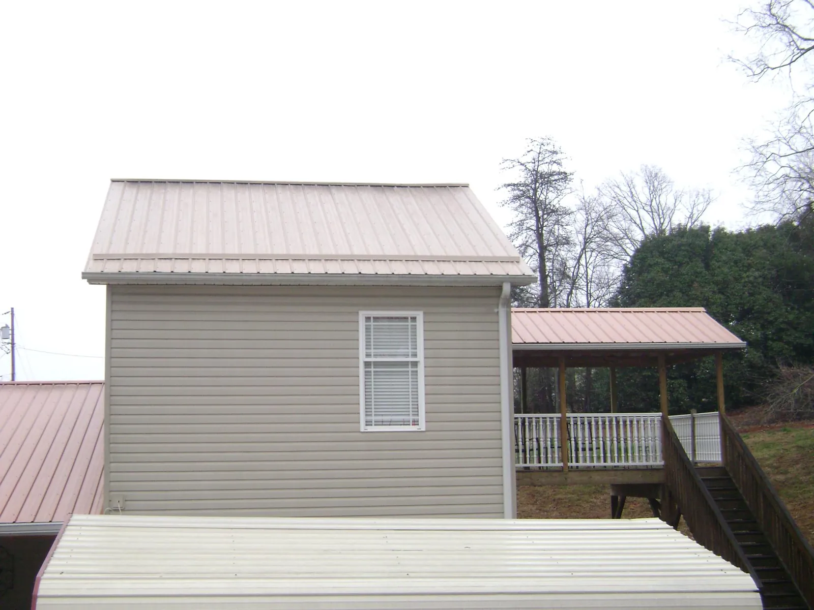 Tan metal roofs on a two story addition and attached porch, from a Roof Replacement job in Whitinsville